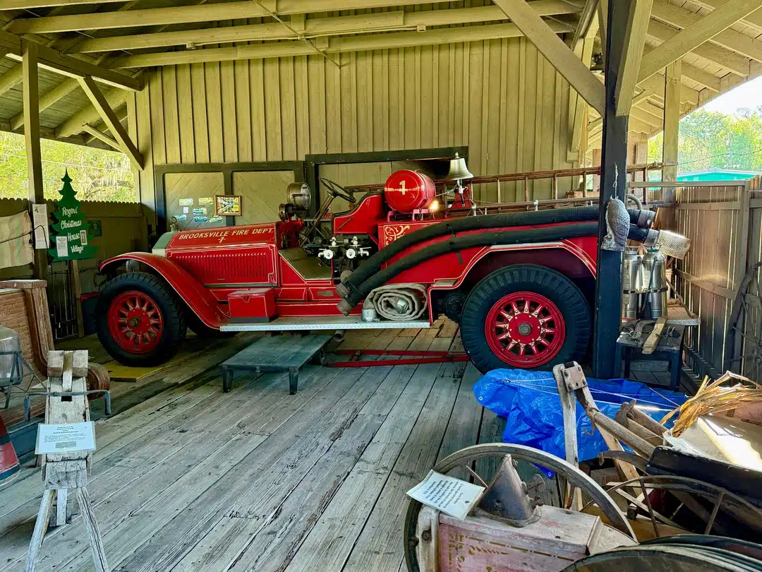 An old bright red fire engine parked under a wooden balcony.