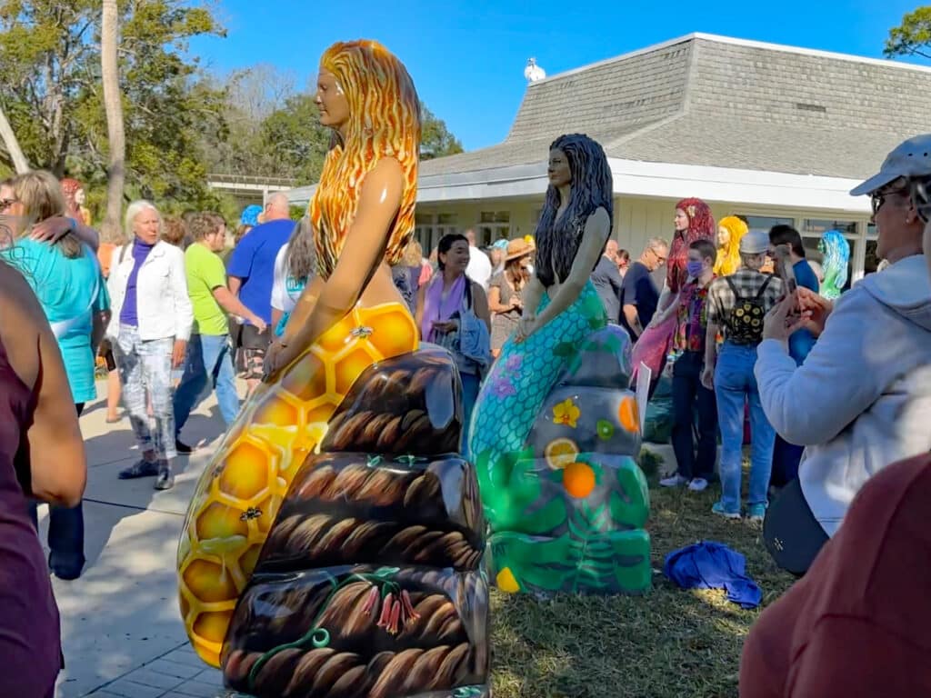 A crowd of people take photos and look at the mermaid statues during the Unveiling Day at Weeki Wachee Springs State Park