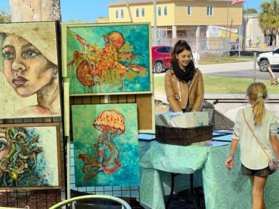 Artist Renata displaying whimsical paintings in her booth at the Front Porch Art Walk in Hernando Beach, FL.