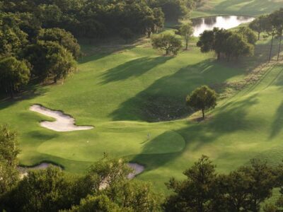 An aerial view of 'The Roost' golf course at Cabot Citrus Farms, featuring rolling green hills dotted by oak trees.