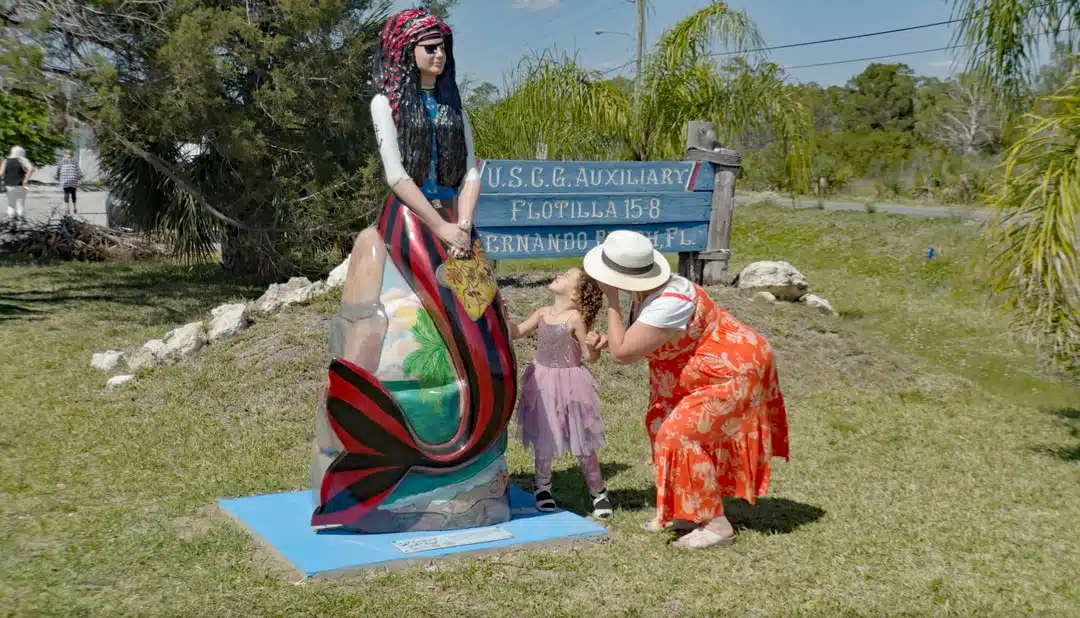 A woman and girl take a closer look at the artwork on a painted mermaid statue.